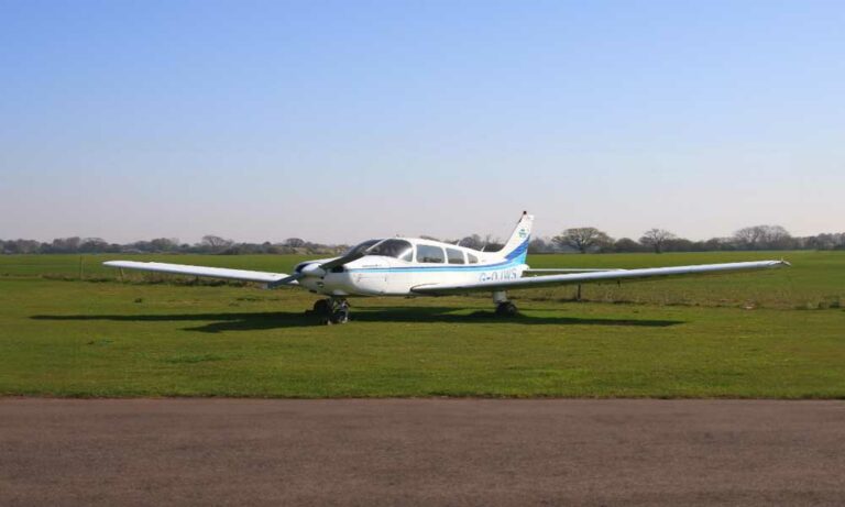 Small white airplane parked on grassy airfield