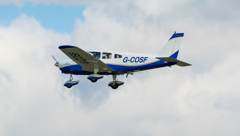 Blue and white G-COSF aircraft flying in cloudy sky
