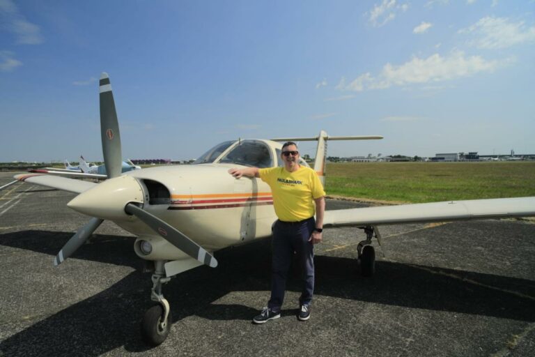 Man smiling next to small airplane on sunny day