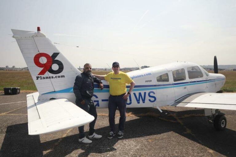 Two men standing beside a Piper airplane on tarmac