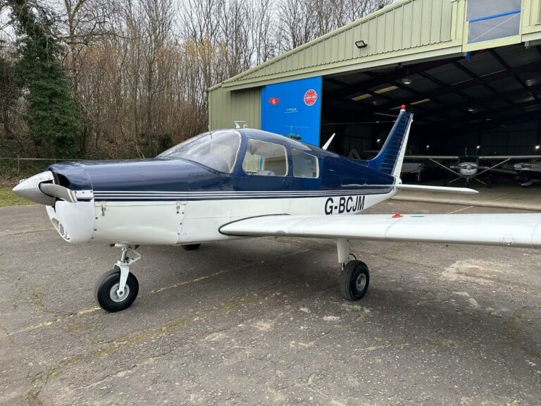 Blue and white aircraft parked outside hangar, registration G-BCJM