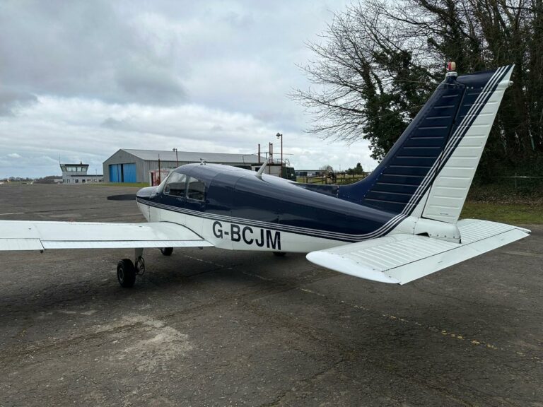 Single-engine plane parked at airfield under cloudy sky
