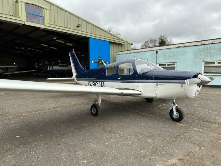 Blue and white small aircraft parked outside hangar