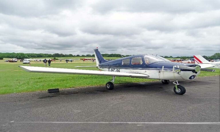 Small aircraft at grassy airfield with cloudy sky