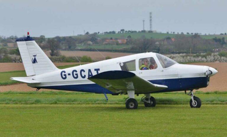 Small aircraft labeled G-GCAT landing on grassy field